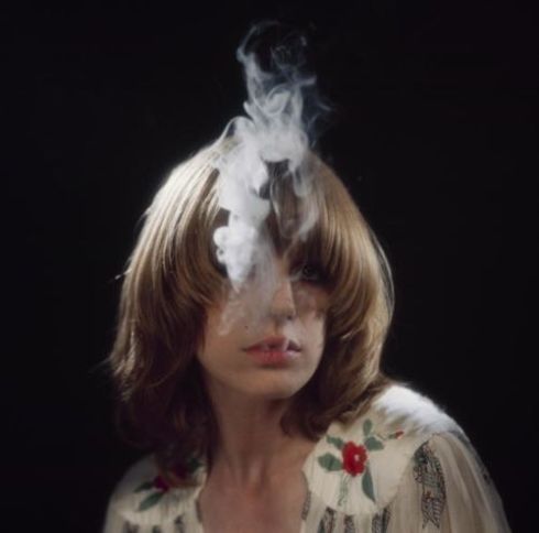 Singer Marianne Faithfull blows smoke from her mouth as she poses in a dress by Ossie Clark in 1973.